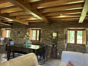 Ein Zimmer mit Steinwänden und Holzbalkendecke, einem Esstisch, Stühlen, einer Uhr und einem Sofa.