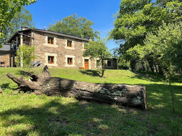 Ein Steinhaus mit einer Veranda, umgeben von Bäumen und einem Baumstamm im Vordergrund.