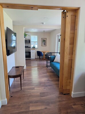 Ein modernes Interieur mit Holzboden, einer Essecke mit blauem Sofa, einem an der Wand montierten Fernseher und einer Küche im Hintergrund.