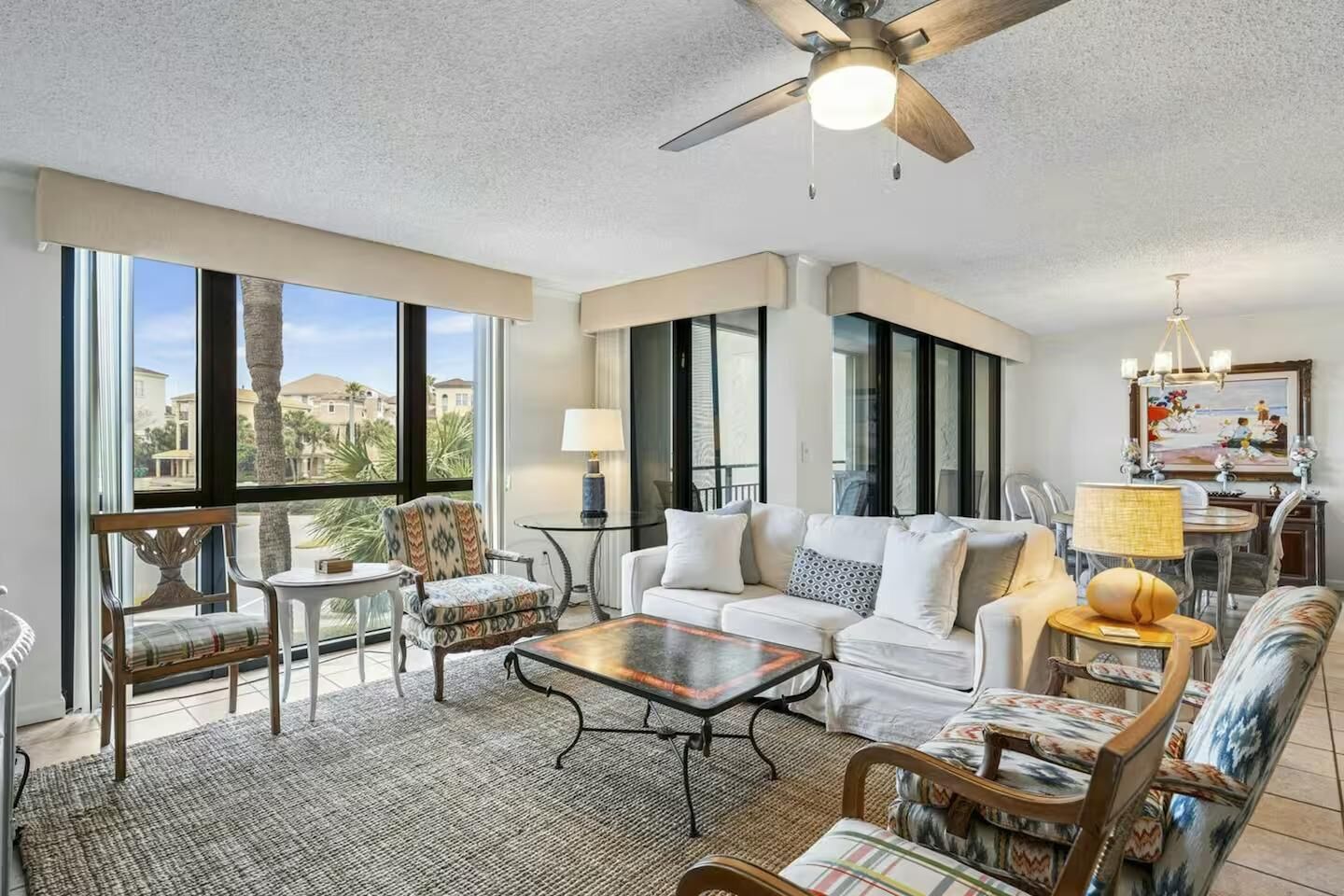 A spacious living room with a large window, a ceiling fan, and a dining area with a chandelier.