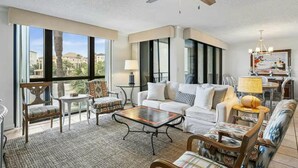 A spacious living room with a large window, a ceiling fan, and a dining area with a chandelier. - Enclave 203b (Destin)