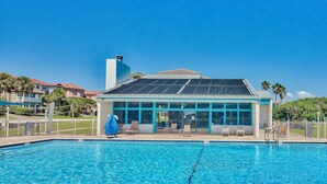 A swimming pool with a sunshade, lounge chairs, and a building with large windows and a solar panel roof. - Enclave 203b (Destin)