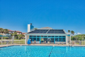 Ein Schwimmbecken mit Sonnenschirm, Liegestühlen und einem Gebäude mit großen Fenstern und einer Solardach.