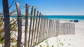 Ein Strand mit Holzzaun, klarem blauen Wasser und einigen Liegestühlen.