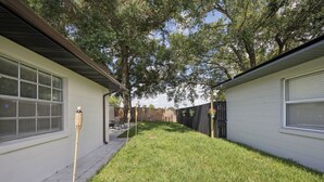Un patio trasero residencial con césped, valla de madera y una casa con ventana y puerta.