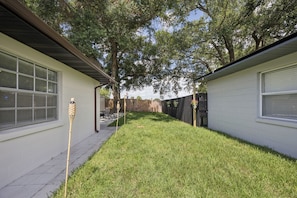 A residential backyard with a lawn, a wooden fence, and a house with a window and a door.