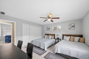 A hotel room with two beds, a ceiling fan, a dining table, and a blue chair.