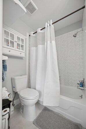 A bathroom with a toilet, bathtub, shower curtain, and a cabinet with glass doors.