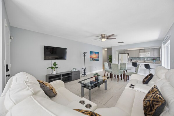 A modern living room with a sofa, coffee table, TV, and a dining area with chairs and a table.