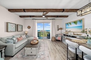 A living room with a sofa, coffee table, and bar seating. There is a balcony with a view. - Beach Resort 501 (Miramar Beach)