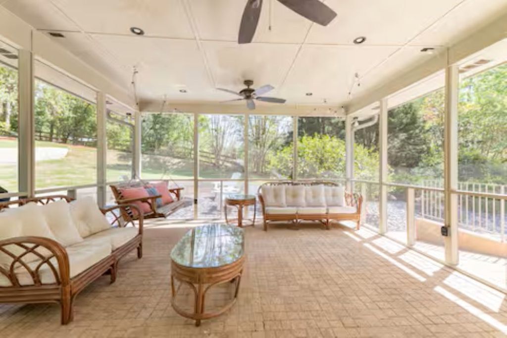 A covered patio with wicker furniture, a glass table, and a ceiling fan.