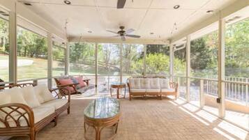 A covered patio with wicker furniture, a glass table, and a ceiling fan.