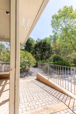 Un espace extérieur doté d’un chemin pavé, d’une rambarde en métal et offrant une vue sur des arbres et des arbustes.