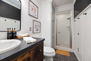 Un bagno con lavandino bianco, piano di appoggio scuro, mobile contenitore in legno, due immagini floreali incorniciate e zona doccia con porta in vetro.