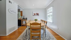 A dining area with a round table, chairs, a rug, a kitchen in the background, and a wall sign. - The Park House I Family Retreat Near Fort Benning & Auburn (Columbus)