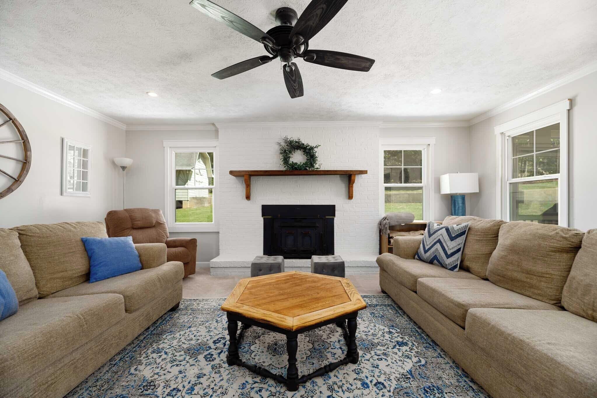 A living room with two sofas, a coffee table, a fireplace, and a ceiling fan.
