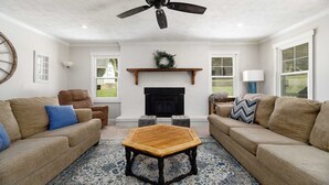 A living room with two sofas, a coffee table, a fireplace, and a ceiling fan. - The Park House I Family Retreat Near Fort Benning & Auburn (Columbus)