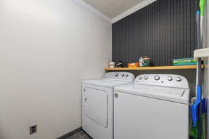 Une buanderie avec un lave-linge et un sèche-linge blancs, une étagère contenant divers objets et un mur noir à motifs.