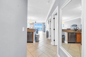 A modern kitchen with a view, a dining area, and a hallway leading to a balcony. - Twin Palms 801 (Panama City Beach)