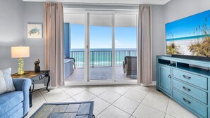 Una stanza con un balcone, un divano, un mobile TV e un quadro raffigurante una spiaggia.