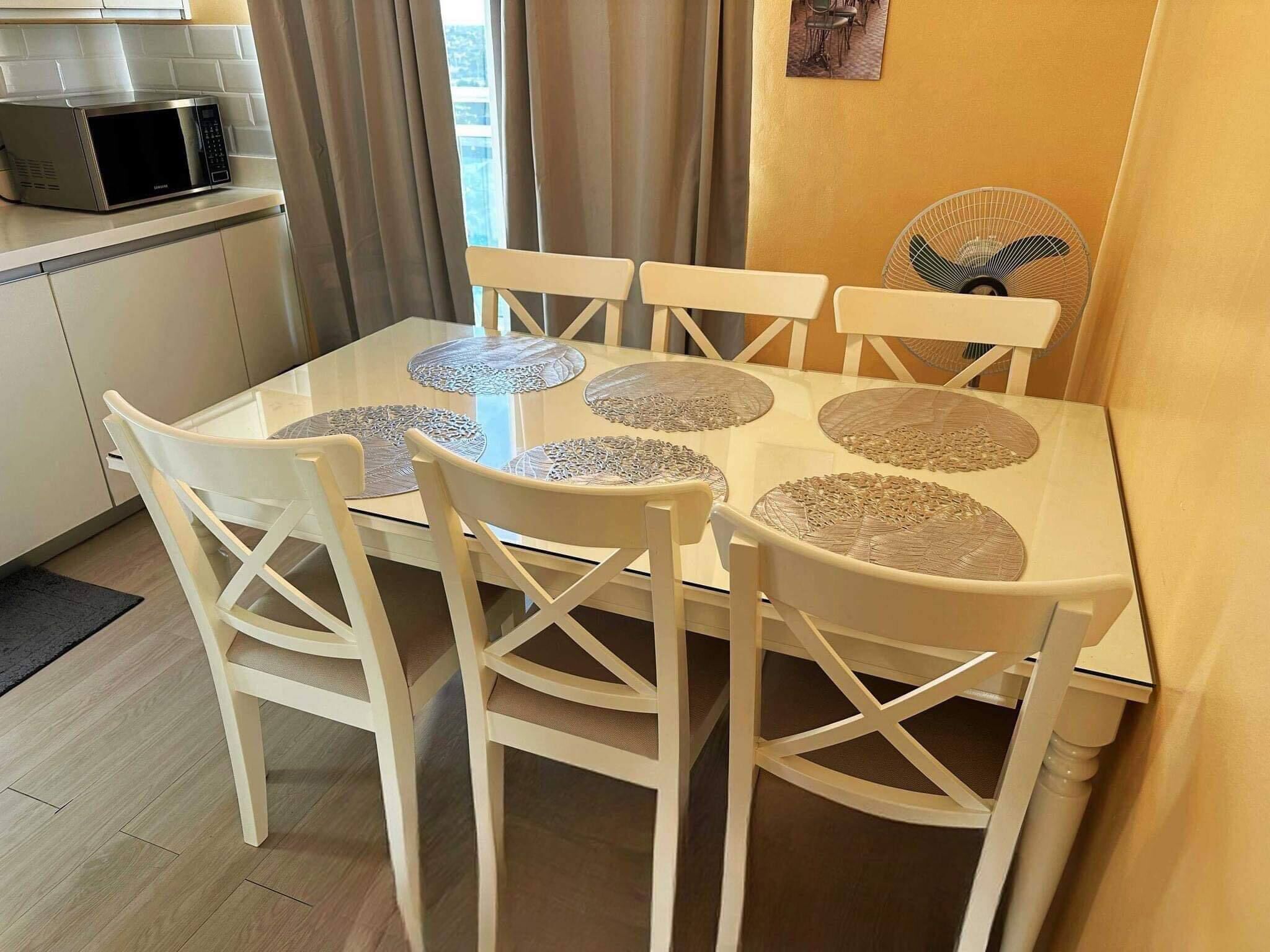 A dining area with a glass table, white chairs, and a microwave in the background.
