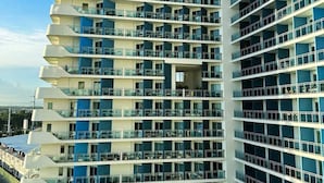 Un edificio de gran altura con varios balcones, cielo despejado y una carretera al frente.
