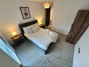 A neatly made bed with pillows and a blanket, a bedside lamp, a framed artwork on the wall, and a wooden wardrobe. -  2-Bed, 2-Bath Apartment in the Heart of York City Centre with secure parking (York)