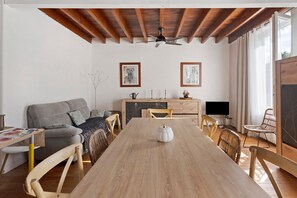 Ein geräumiger Wohnbereich mit Esstisch aus Holz, einer Couch und einem Fernseher.