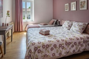 Une chambre à coucher avec un grand lit, un plus petit lit, un bureau et une fenêtre avec des rideaux.