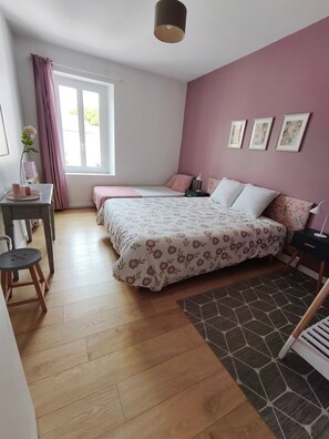 Une chambre avec deux lits, un bureau, une chaise, une fenêtre avec des rideaux et un mur décoré de tableaux encadrés.