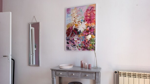 Een kamer met een grijze bureau, een spiegel, een radiator en een bloemrijk schilderij aan de muur.