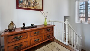 A wooden dresser with drawers, a vase with branches, and a painting on the wall.