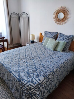 Een bed met een bedspreider met een geometrisch patroon, een bedlamp en een wandspiegel.
