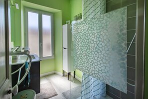 Un baño con pared verde, cabina de ducha de vidrio, lavabo con espejo y ventana.