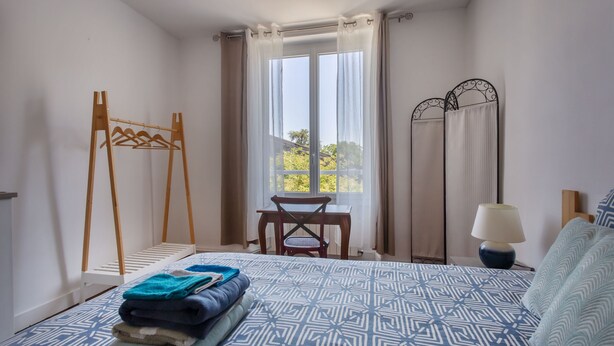 Una camera da letto con un letto, un appendiabiti in legno, un tavolo e una finestra con tende.