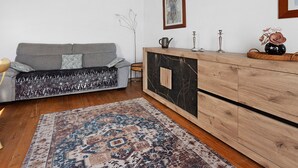 Un soggiorno con un divano grigio, cuscini decorati, un mobile in legno, un tappeto e un quadro appeso al muro.