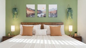 Ein Bett mit weißer Bettdecke, zwei braunen Kissen und einem hölzernen Kopfteil. Drei an der Wand befestigte Landschaftsbilder sind zu sehen.