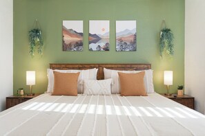 A bed with a white bedspread, two brown pillows, and a wooden headboard. There are three wall-mounted paintings depicting landscapes. - Stylish Tempe Stay ~ Swimming Pool, King Bed! (Tempe)