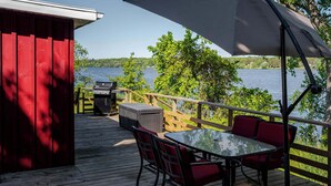A wooden deck with a table and chairs, a grill, and a large umbrella. - Hay Bay Hytte - Waterfront Cottage (Greater Napanee)
