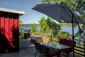 Eine Holzterrasse mit Tisch, Stühlen, einem Grill und einem großen Sonnenschirm.