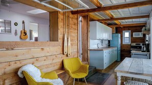 A wooden interior with a kitchen, yellow chairs, a dining table, and a guitar on the wall. - Hay Bay Hytte - Waterfront Cottage (Greater Napanee)