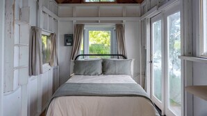 A bedroom with a bed, curtains, a window, and a thermostat. - Hay Bay Hytte - Waterfront Cottage (Greater Napanee)