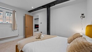 Quarto com cama, porta de madeira, janela com cortinas, televisão e luminária fixada na parede.