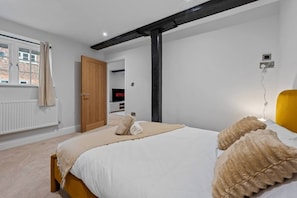 A bedroom with a bed, a wooden door, a window with curtains, a television, and a wall-mounted light. - Modern & Historic Mill Flat with Stream Views (Surrey)