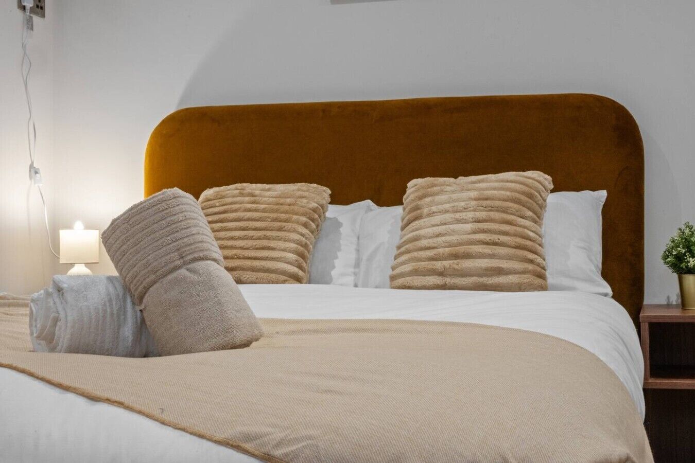 A neatly made bed with a headboard, a bedside lamp, and a small potted plant on the nightstand.