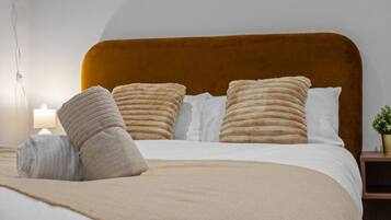 A neatly made bed with a headboard, a bedside lamp, and a small potted plant on the nightstand.
