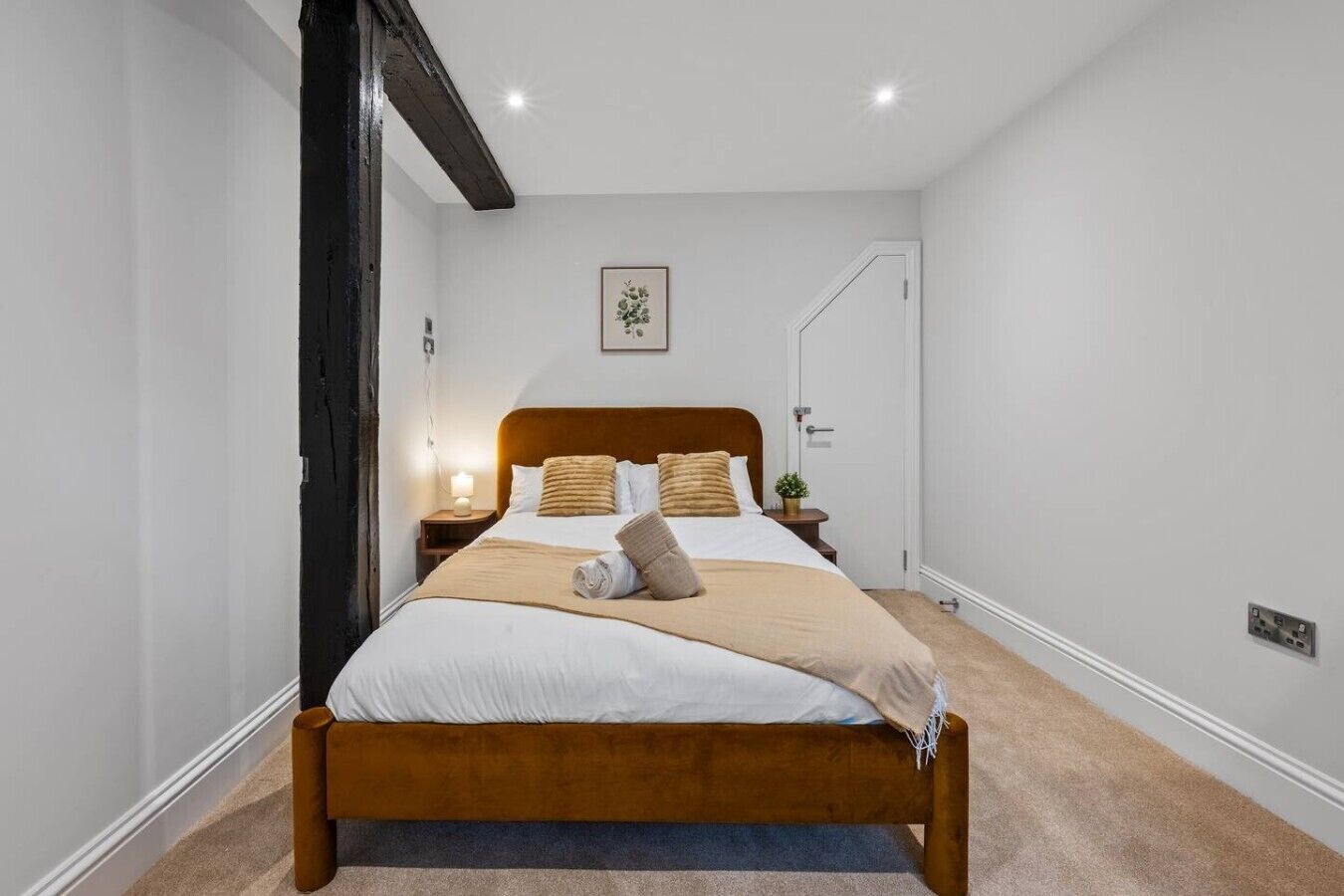 Uma cama bem arrumada com cabeceira de madeira, mesa de cabeceira com abajur e um quadro na parede.