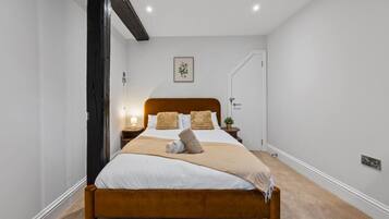 Uma cama bem arrumada com cabeceira de madeira, mesa de cabeceira com abajur e um quadro na parede.