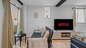Uma sala de estar moderna com sofá, TV exibindo 'NETFLIX', uma mesa pequena e uma janela com cortinas.
