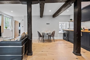 A modern kitchen with a washing machine, a dining area with a table and chairs, and a seating area with a sofa. - Modern & Historic Mill Flat with Stream Views (Surrey)